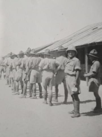 Men standing in line in army uniforms. One man looks at the camera.